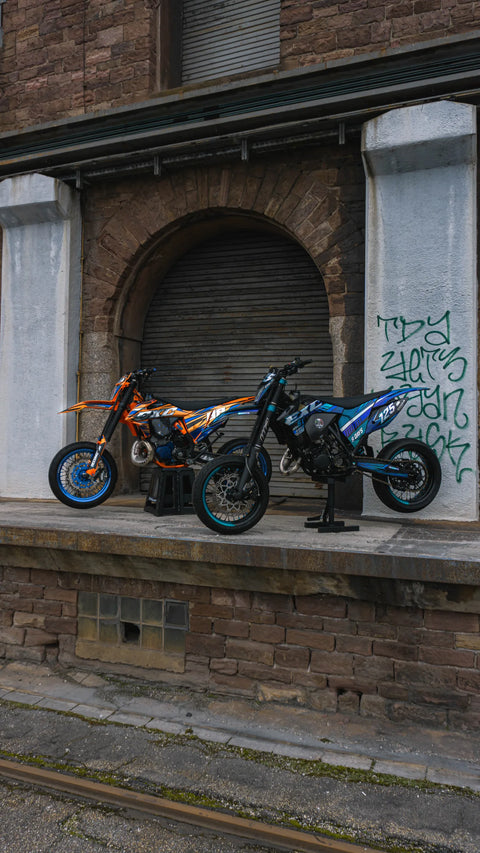 Dos supermotards lado a lado con kits de adhesivos naranja y azul