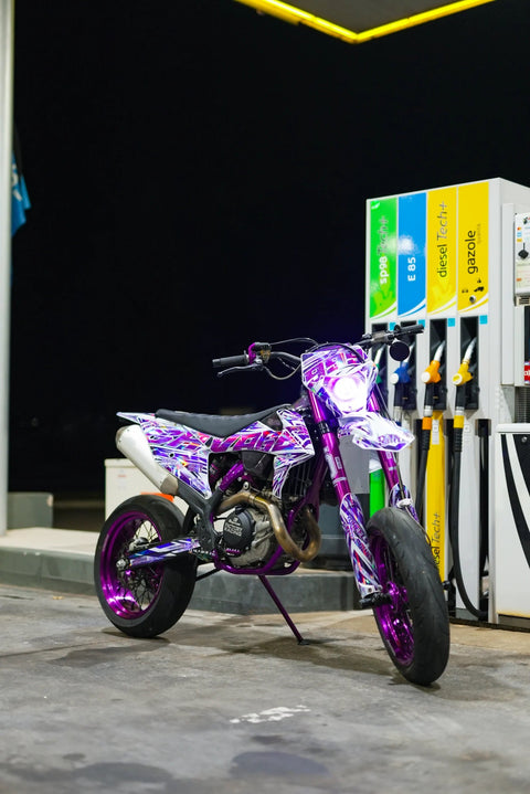 Supermotard violet photographié de nuit devant une station-service