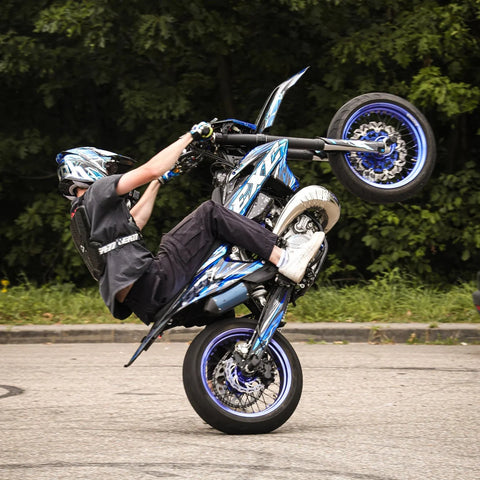 Piloto con casco haciendo un caballito sobre un supermotard azul y blanco