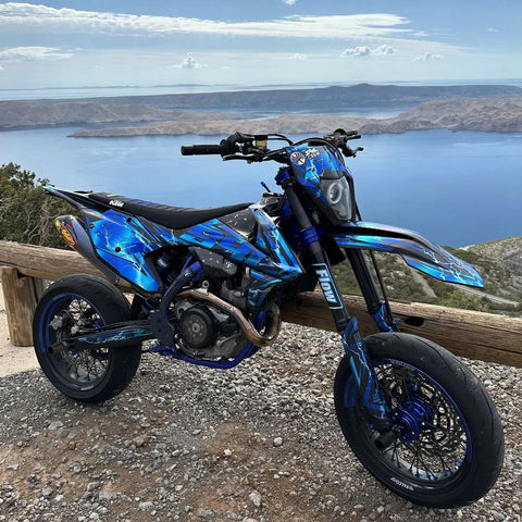 Supermotard bleu au kit déco multicolore face à un paysage côtier